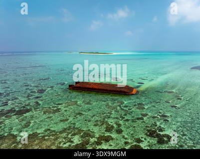 Aus der Vogelperspektive auf einen versunkenen, rostigen Binnenkahn, der im flachen türkisfarbenen Wasser ruht, mit einer kleinen Insel in der Ferne, Hoarafushi, Thiladhunmathee Uthurub Stockfoto