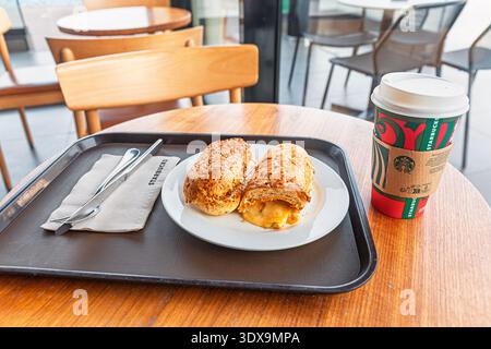 5. Dezember 2025, Abu Dhabi, VAE: Starbucks Weihnachtsbecher mit einem Frühstückssandwich auf weißem Teller und schwarzem Tablett, bereit für das morgendliche Essen Stockfoto