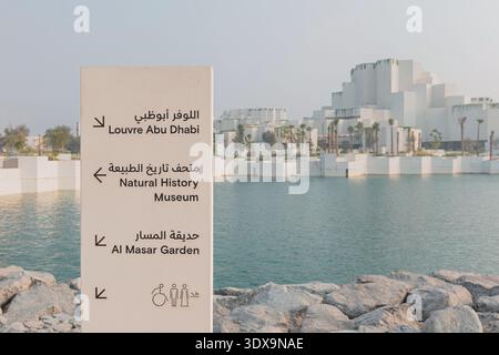 6. Dezember 2025, Abu Dhabi, VAE: Wegweiser mit dem Louvre, dem Naturkundemuseum und dem Al Masar Garden, mit moderner Architektur und Stockfoto