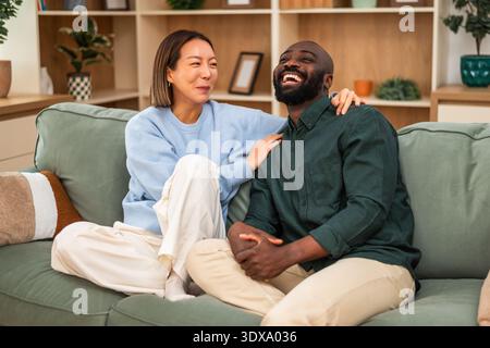 Zwei Partner kuscheln sich auf eine Couch und lächeln hell, während sie die Gesellschaft des anderen in einem stilvollen und einladenden Ambiente genießen. Stockfoto