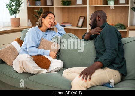 Erwachsenes multirassisches Paar, das zu Hause auf dem Sofa sitzt und über ihre gesundheitlichen Probleme spricht. Stockfoto