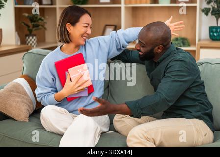 Fröhliches, multirassisches Paar hat zu Hause Spaß beim Austausch von Geschenken. Stockfoto