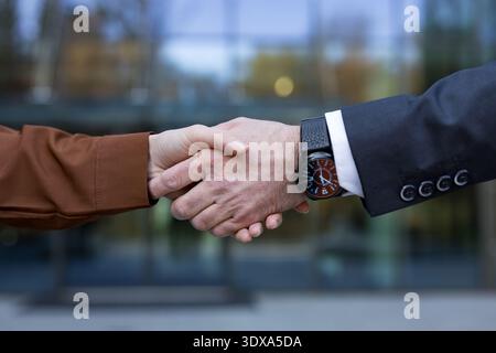 Zwei Geschäftsleute schütteln die Hand und symbolisieren Partnerschaft, Vereinbarung, Vertrauen und erfolgreiche Zusammenarbeit außerhalb eines modernen Unternehmensgebäudes Stockfoto