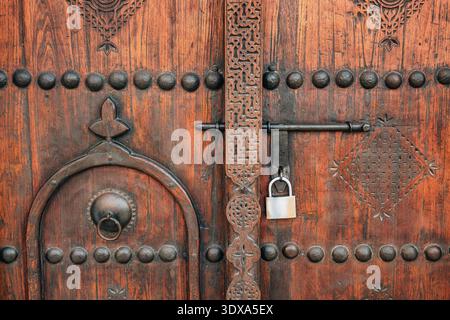 Rustikale Eingangstür aus Holz mit Nieten-Metalldetails, einem Messingklopfer und einem antiken Schloss. Traditionelle Handwerkskunst Stockfoto