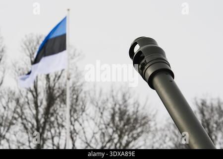 Estnische Nationalflagge winkt im Wind hinter einer militärischen Artillerie-Fass-Mündungsbremse, die Verteidigung, nationale Sicherheit und Macht der Armee symbolisiert. Stockfoto