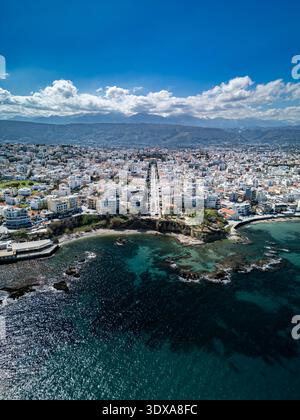 Aus der Vogelperspektive trifft das türkisfarbene Wasser auf die zerklüftete Küste, im Kontrast zu den weißen Gebäuden unter hellem Himmel, Chania, Griechenland. Stockfoto