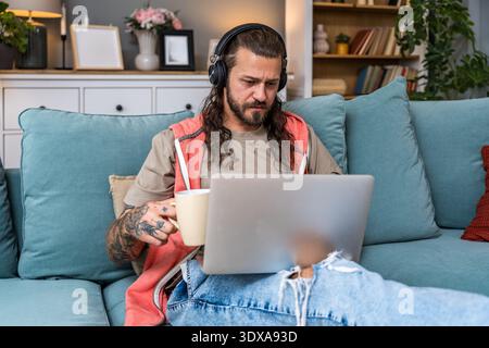 Freiberuflicher KI-Experte, der aus der Ferne arbeitet, Kaffee trinkt, während er Laptop und Kopfhörer verwendet, konzentriert sich auf Innovationsberatung, digitale Strategie und Expat l l Stockfoto