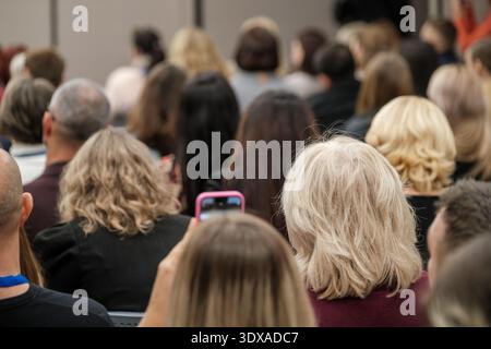 Das Publikum sitzt in Reihen bei einer Indoor-Konferenz, die Teilnehmer hören und zeichnen Präsentationen mit dem Smartphone auf, engagierte sich für professionelle Veranstaltungen. Stockfoto
