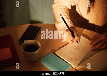 Sonnenlicht, das auf der Hand einer Geschäftsfrau leuchtet, die im Büro mit Bleistift im Tagebuch schreibt Stockfoto