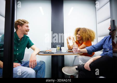 Glückliche männliche und weibliche Geschäftsangestellte machen Pause, während sie in der Bürokabine sitzen Stockfoto