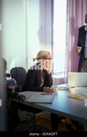 Lächelnde Geschäftsfrau mit Hand am Kinn am Tisch im Besprechungsraum Stockfoto