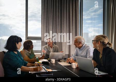 Leitender Geschäftsmann erklärt den Kollegen, die beim Meeting am Tisch sitzen, Strategien Stockfoto