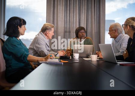 Reife Geschäftsfrau diskutiert Strategie mit Kollegen, während sie am Konferenztisch im Büro sitzt Stockfoto
