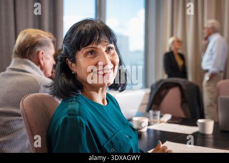 Lächelnde Geschäftsfrau, die wegblickt, während sie im Besprechungsraum sitzt Stockfoto