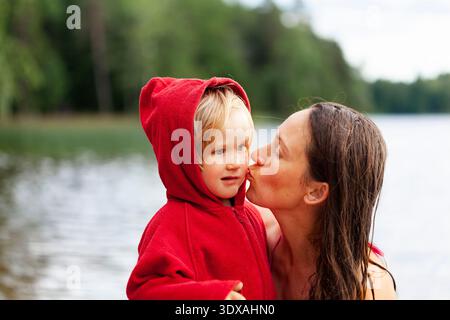 Frau, die ihre Tochter am See küsst Stockfoto