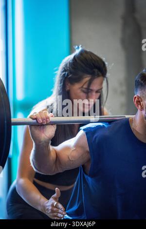Muskulöser männlicher Athlet, der Squats mit Frau im Fitnessstudio macht Stockfoto