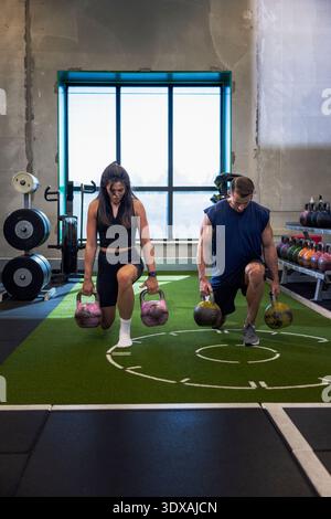 Volle Länge von männlichen und weiblichen Athleten, die Ausfallschritte mit Kettlebell im Fitnessstudio machen Stockfoto