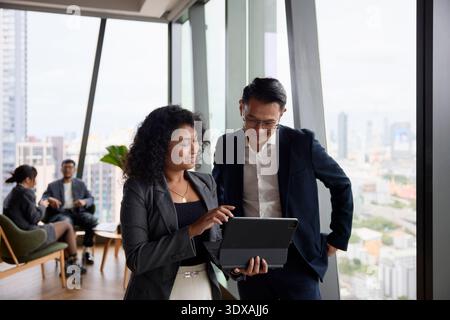 Lächelnde Mitarbeiterin zeigt dem Manager im Büro ein digitales Tablet Stockfoto