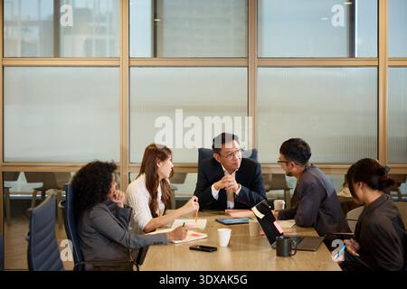 Manager hört Kollegen zu, während sie im Büro um den Tisch sitzen Stockfoto