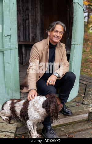 Voller Länge eines lächelnden älteren Mannes, der mit Hund auf Holztreppen sitzt Stockfoto