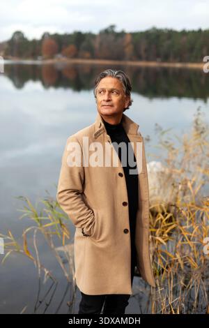Ein älterer Mann posiert mit Händen in Taschen am See Stockfoto
