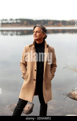 Modischer Mann posiert mit Händen in Taschen nahe dem See Stockfoto