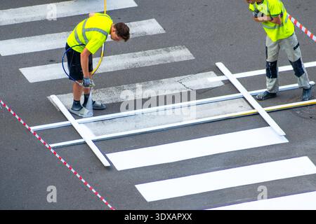 Straßenarbeiter lackieren Linien auf Asphalt. Arbeiter Lackieren Fußgängerübergänge. Anwenden der weißen Farbe der Straßenmarkierungen. Straßenbahnmarkierung funktioniert. Ukraine, Kiew - 14. August 2025 Stockfoto