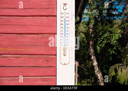 Klassisches analoges Außenthermometer auf rustikaler roter Holzfassade, das milde Sommertemperaturen in Schwedisch Lappland, arktisches Sommerklima, TRA anzeigt Stockfoto