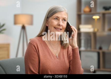 Lächelnde Seniorin, die zu Hause mit dem Smartphone auf dem Sofa spricht Stockfoto