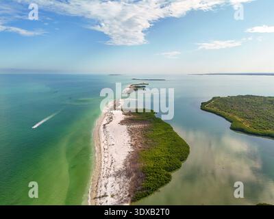 Aus der Vogelperspektive auf den unberührten weißen Sand der Honeymoon Island, der auf das smaragdgrüne Wasser trifft, ein Boot, das durch die Wellen in Richtung Festland, Dunedin, Flo fährt Stockfoto