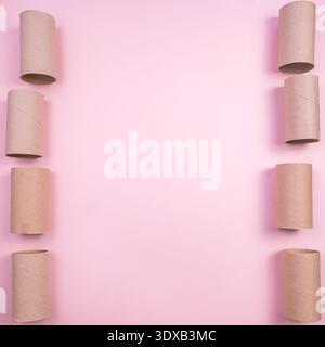 Leere Toilettenpapierröhrchen aus Pappe, kreisförmig angeordnet auf rosa Hintergrund. Die Szene ist minimalistisch und betont die Textur der tu Stockfoto