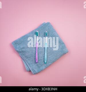 Zwei Zahnbürsten auf einem grauen Handtuch vor rosa Hintergrund. Eine Zahnbürste hat einen blauen Kopf und die andere einen rosafarbenen Kopf. Einfaches und sauberes Badezimmer Stockfoto