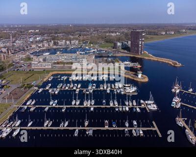 Aus der Vogelperspektive der Boote, die im Yachthafen angedockt sind und die Farben des Himmels reflektieren, mit einem Leuchtturm, der Wache steht, während die Stadt auf den Rand des Wassers trifft, Marina, Alm Stockfoto