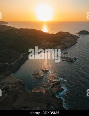 Aus der Vogelperspektive auf die goldene Sonne, die die zerklüftete Küste und das türkisfarbene Wasser des Mittelmeers, Ciutadella, Balearen, Spanien küsst. Stockfoto