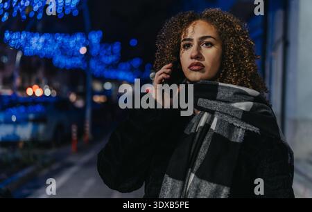 Porträt einer Frau am Telefon bei Nacht unter blauer Stadtbeleuchtung Stockfoto