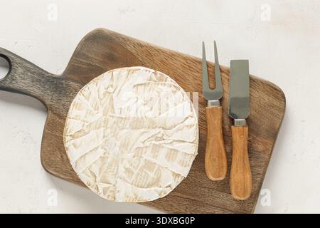 Brie-Käse mit Küchenutensilien auf einem hölzernen Küchenbrett, Nahaufnahme, Blick von oben. Stockfoto