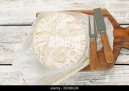 Brie-Käse mit Küchenutensilien auf einem hölzernen Küchenbrett, Nahaufnahme, Blick von oben. Stockfoto