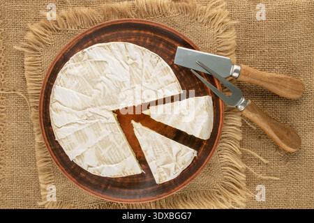 Brie-Käse mit Küchenutensilien auf Jute-Tuch, Nahaufnahme, Blick von oben. Stockfoto