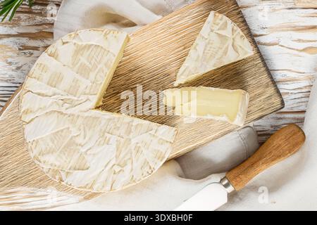 Brie-Käse mit Küchenutensilien auf einem hölzernen Küchenbrett, Nahaufnahme, Blick von oben. Stockfoto