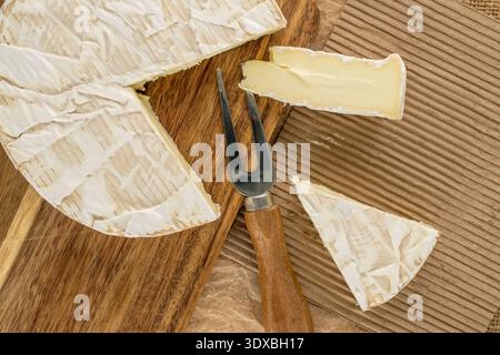 Brie-Käse mit Küchenutensilien auf einem hölzernen Küchenbrett, Nahaufnahme, Blick von oben. Stockfoto
