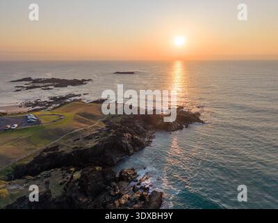Aus der Vogelperspektive auf das strahlende Licht der Sonne, das die zerklüftete Küste küsst, wo dunkle Felsen auf das türkisfarbene Meer treffen, Sawtell, New South Wales, Australien. Stockfoto