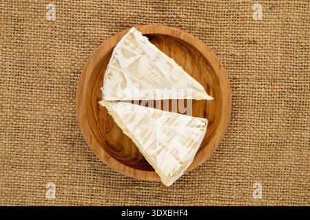Brie-Käse mit Küchenutensilien auf Jute-Tuch, Nahaufnahme, Blick von oben. Stockfoto