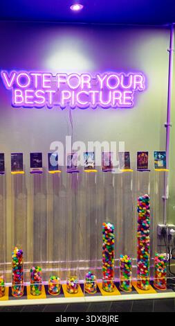 Lebendiges Curzon Soho Kino mit großem rosa Neonschild „VOTE FOR YOUR BEST PICTURE“, farbenfrohen Acrylsäulen mit Süßigkeiten, Filmplakaten und pu Stockfoto