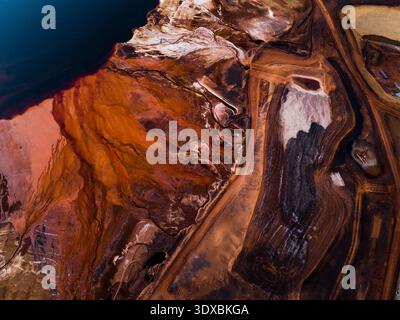 Die Aluminium Refinery, Western Australia, Australien, bietet einen Blick auf feurige Erdtöne und tiefblaues Wasser in einer Industrielandschaft. Stockfoto