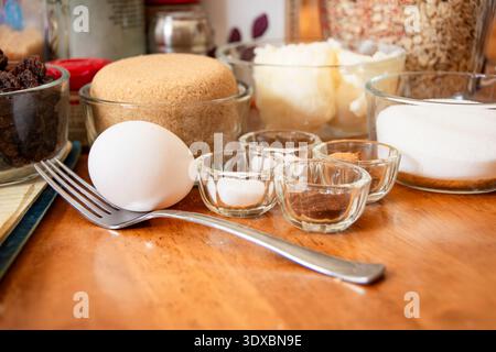 Eine Vielzahl von Backzutaten, darunter ein Ei, Kürzel, Zucker und kleine Glasschalen mit Zehen, Zimt, Salz und Limonade auf einer Holztheke. Stockfoto