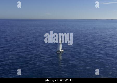 Aus der Vogelperspektive eines einsamen Segelboots, das anmutig auf der ruhigen, tiefblauen Weite des Meeres gleitet, ein ruhiger Kontrast zum klaren Himmel, Alicante, Va Stockfoto