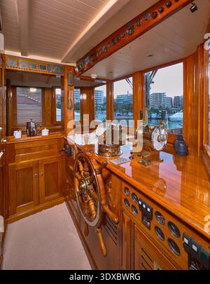 Hölzerner Yachthelm und Navigationsbrücke mit klassischem Rad, Motorsteuerung und Hafenblick Stockfoto