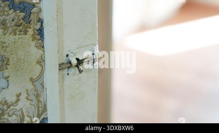 Kleine Schiebetürverriegelung aus Metall an Vintage Holztür mit gemustertem Tapetenhintergrund. Stockfoto