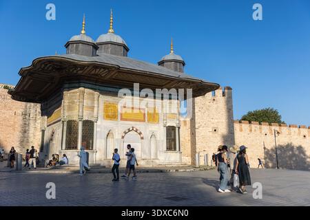 Istanbul, Türkei - 22. August 2024: Kunstvoller osmanischer Brunnen neben den Mauern des Topkapi-Palastes in Istanbul, Türkei. Touristen schlendern und treffen sich um die herum Stockfoto