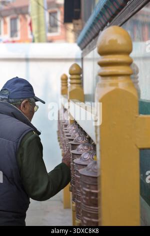 Ein Gläubiger spinnt eine Reihe bronzener Gebetsmühle am Fuße der Boudhanath Stupa in Kathmandu, Nepal. Stockfoto